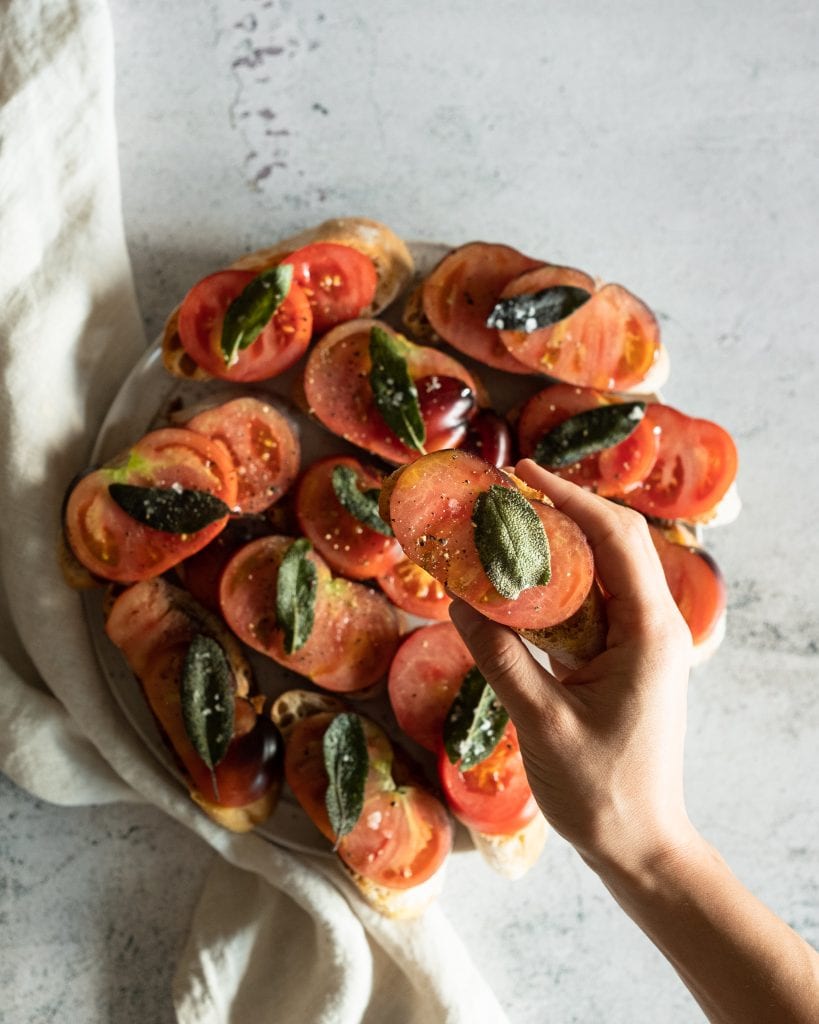 heirloom tomato bruschetta with hand taking one piece from the plate